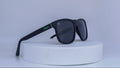 Black sunglasses with green Vybrance logo on a white platform against a white background