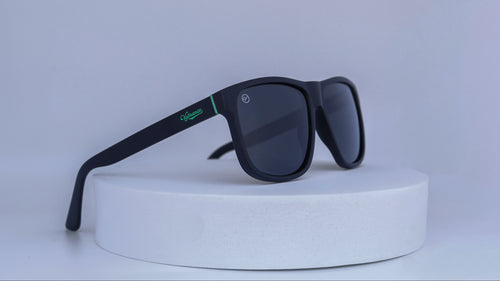 Black sunglasses with green Vybrance logo on a white platform against a white background