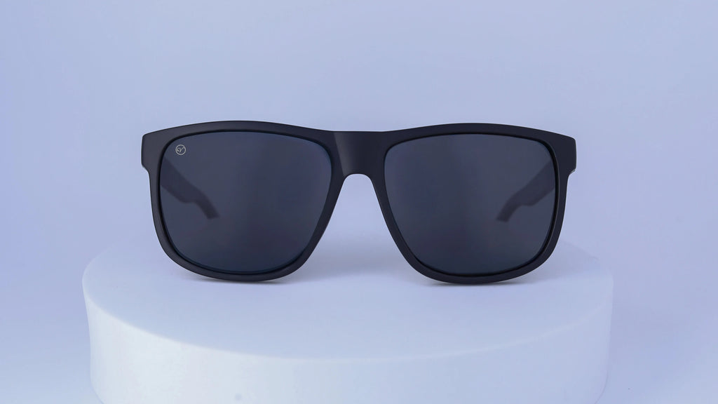 Black sunglasses on a white pedestal against a white background