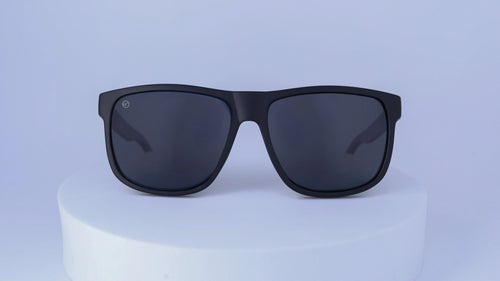 Black sunglasses on a white pedestal against a white background